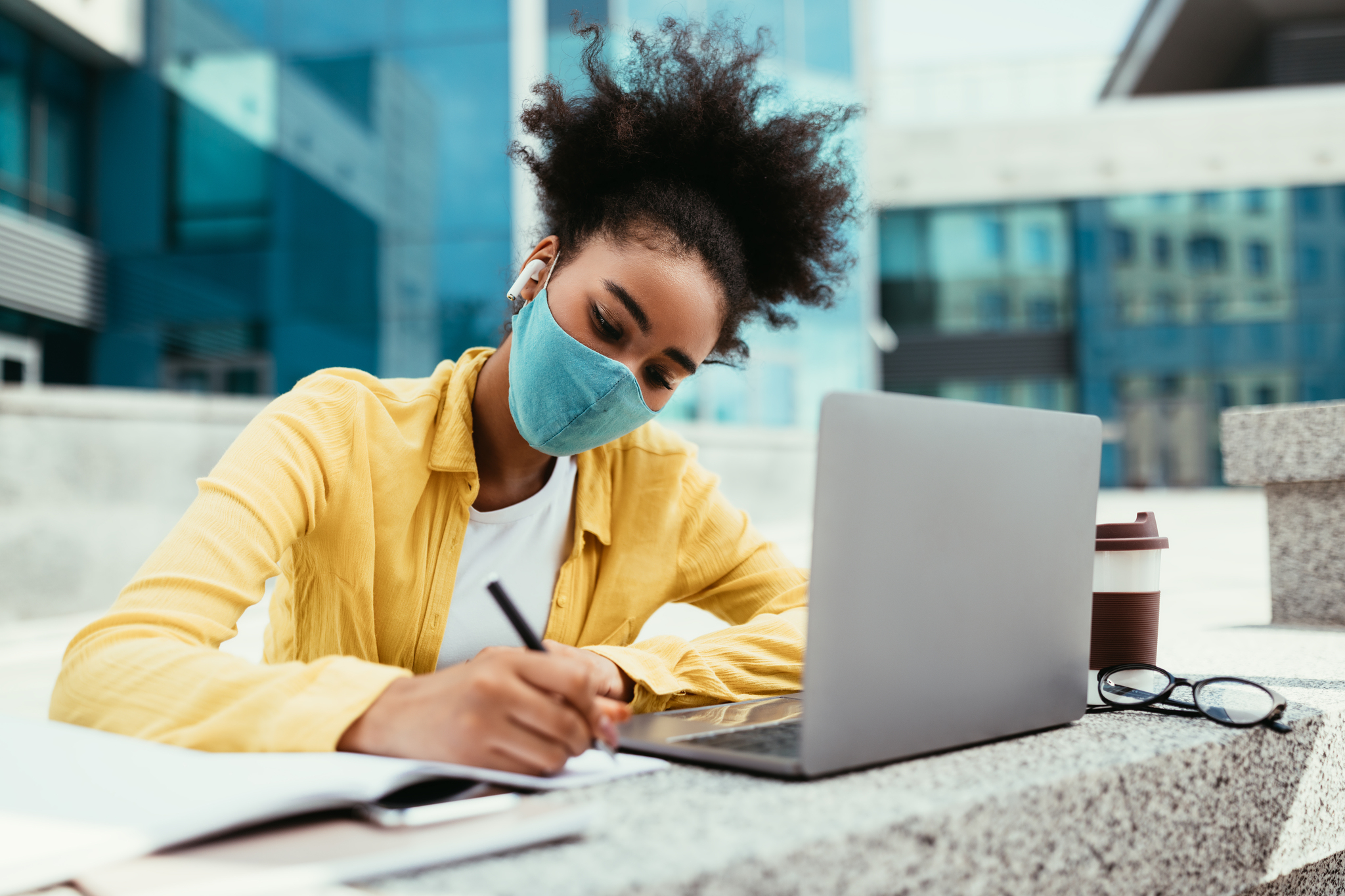 African Teen Girl In Face Mask Learning Using Laptop Computer And Taking Notes Having Remote Lesson Online In Urban College Campus Outside. Student Writing Essay. Modern Education, E-Learning