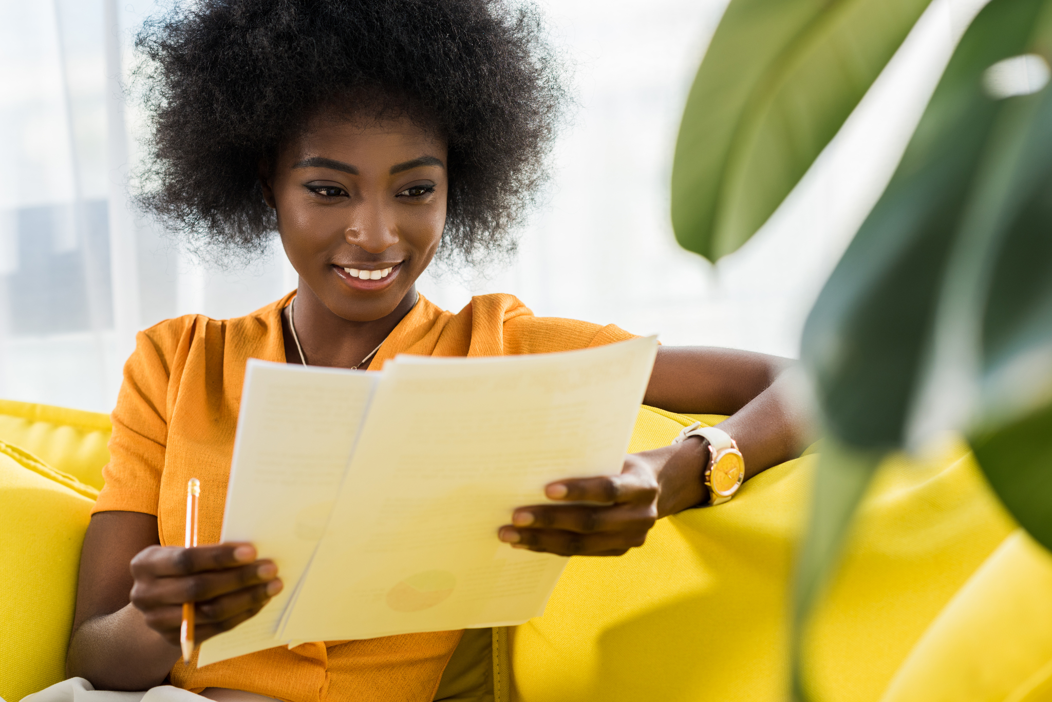 portrait of smiling african american woman with papers remote working on sofa at home